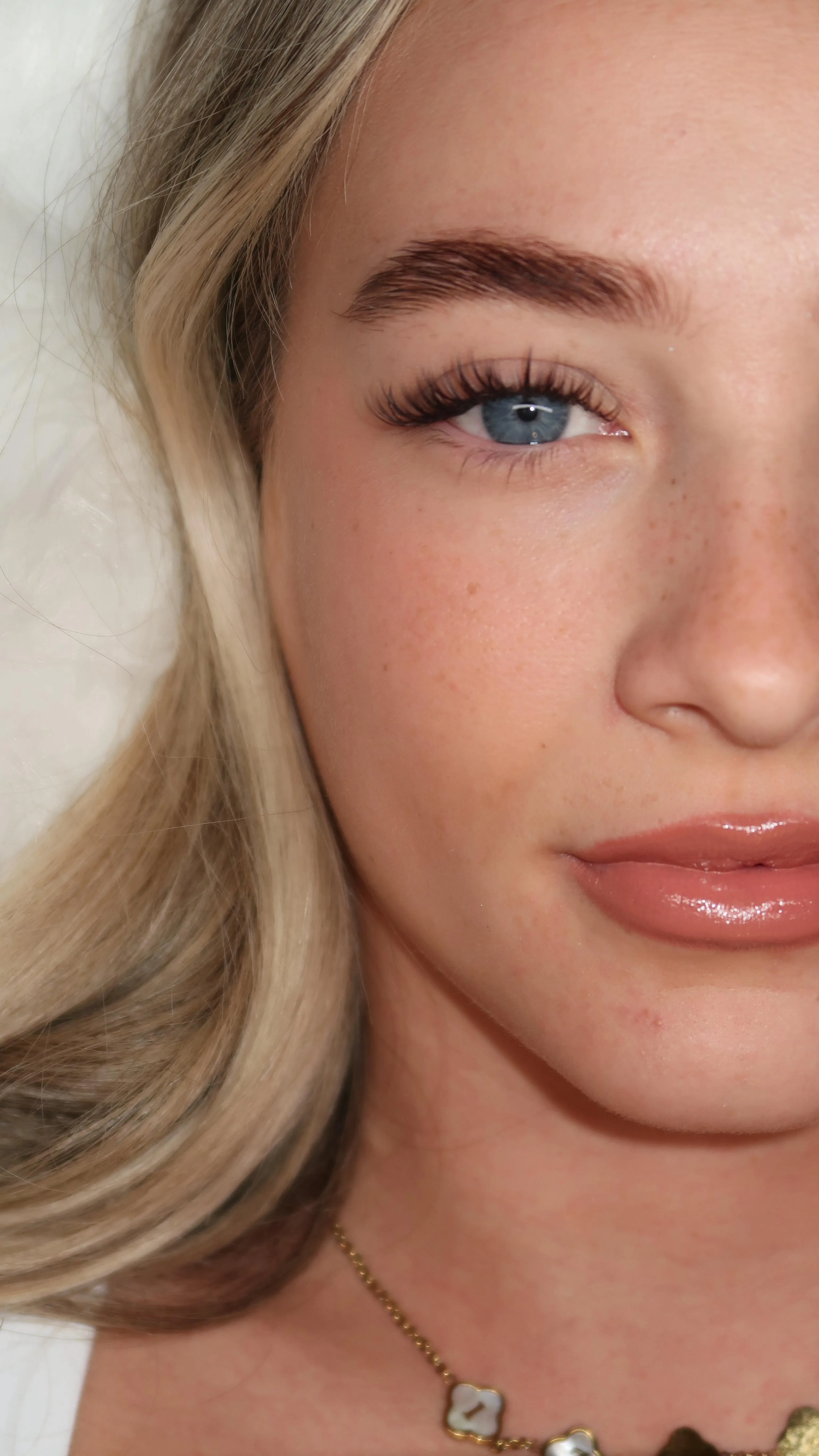 Single blue eye with wispy lashes, glossy nude lip, necklace