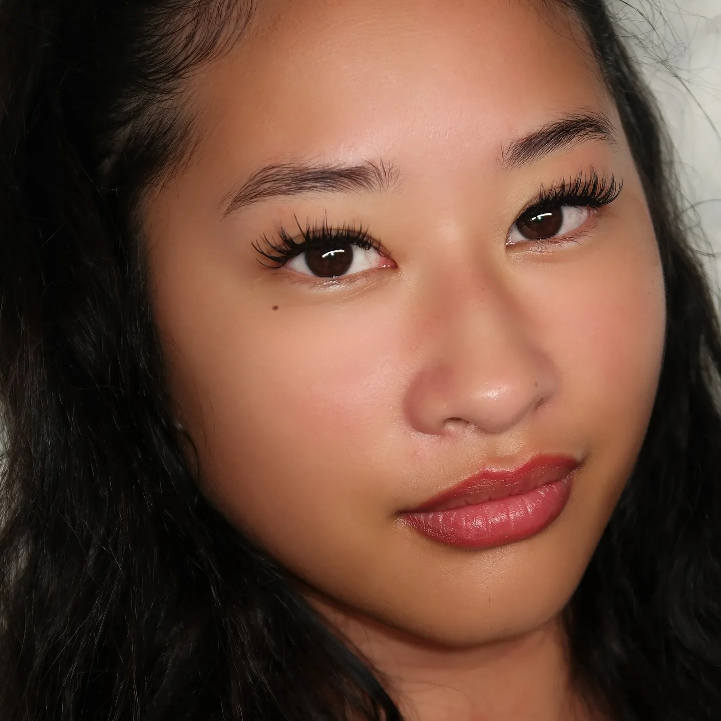 Single brown eye with wispy lash extensions, dark hair, rose lip