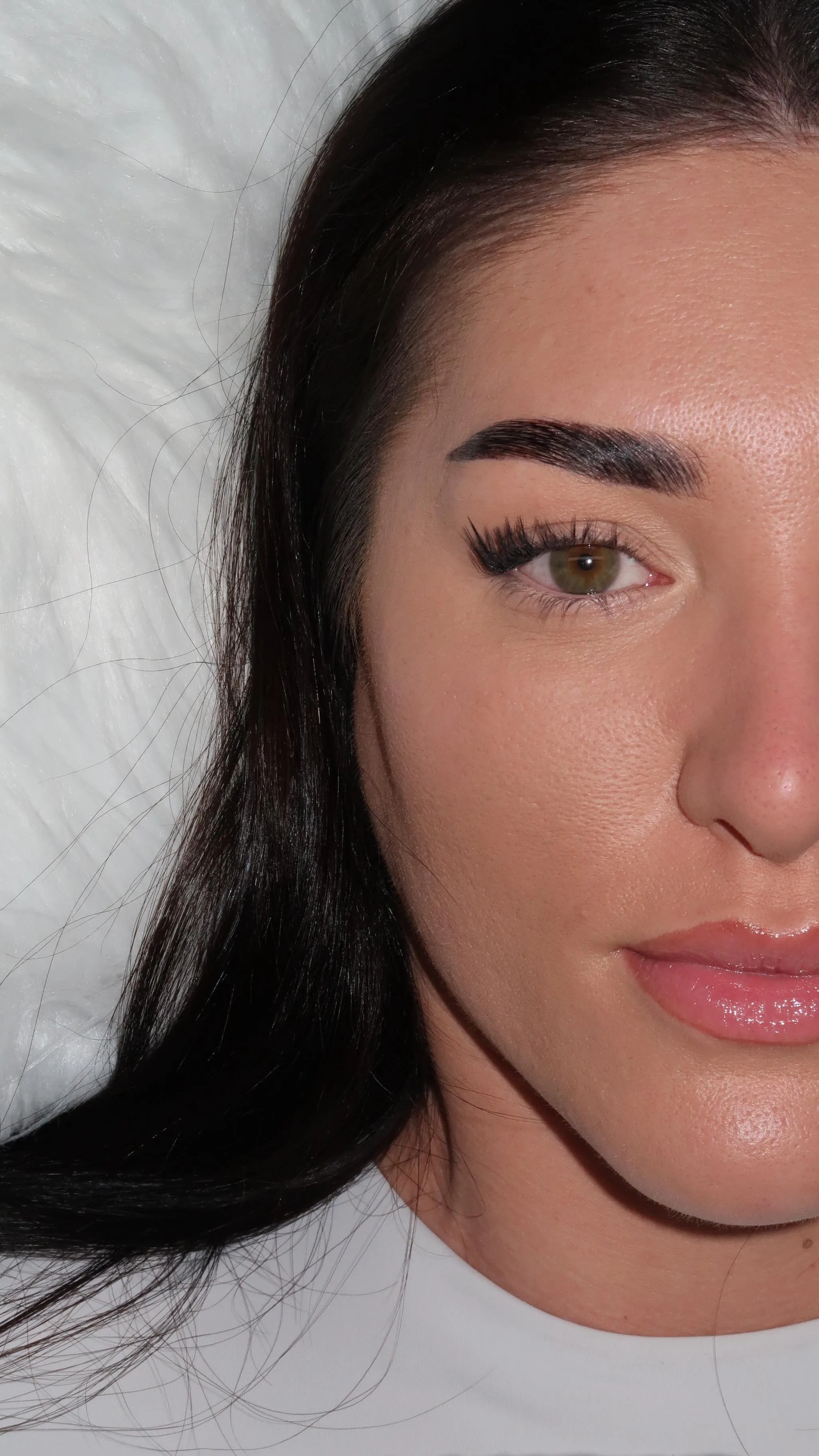 Single hazel eye with wispy lashes, dark hair, bold brow, white fur