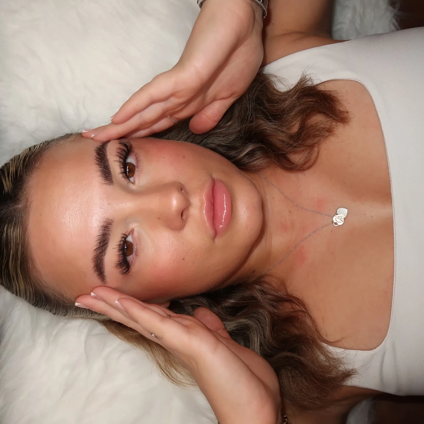 Brunette with hands at face, both brown eyes with wispy lashes, silver necklace