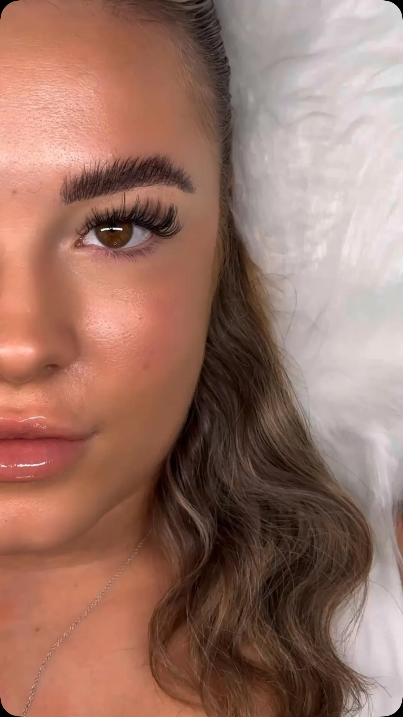 Single brown eye with wispy lash extensions, wavy hair, white fur